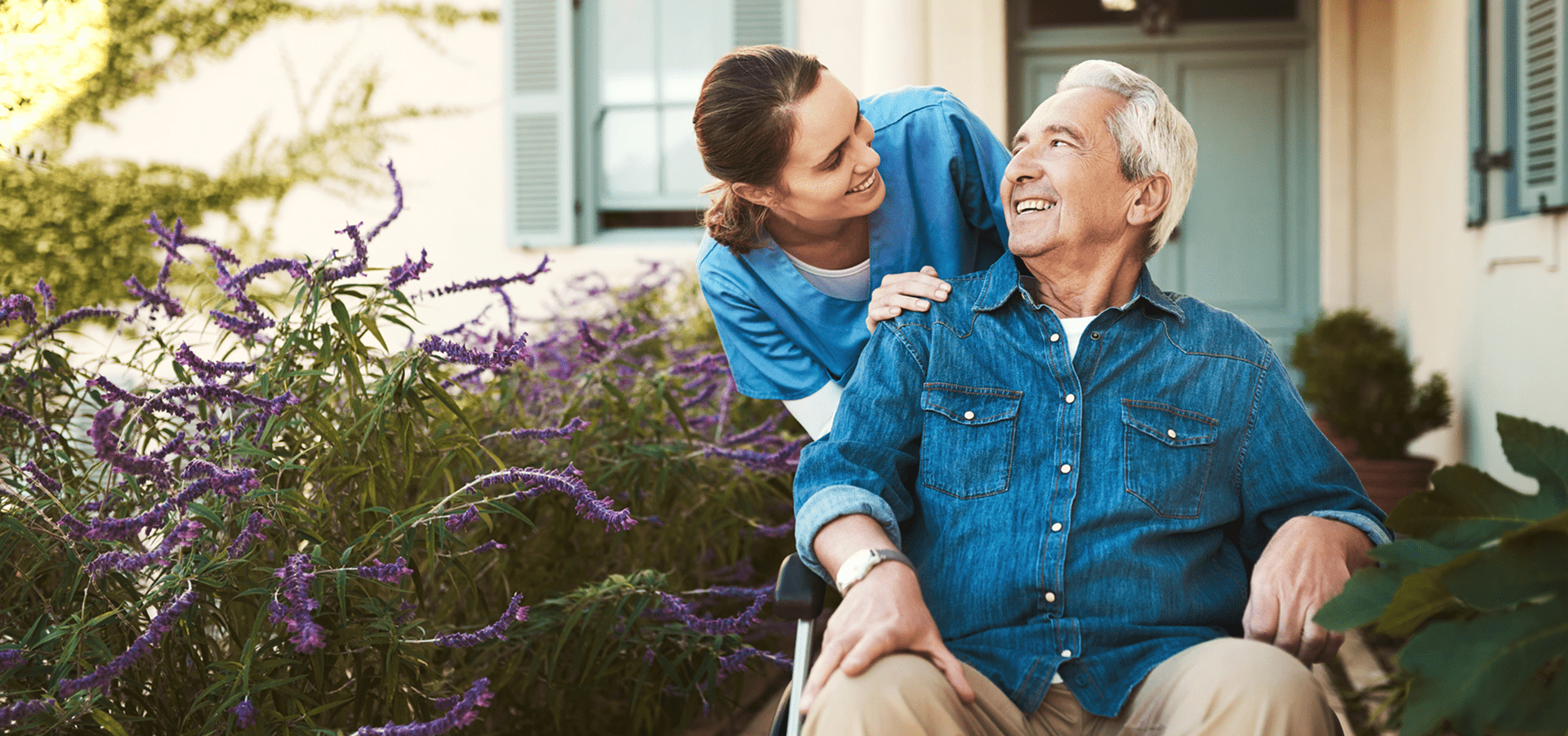Elderly man in wheelchair with smiling caregiver.